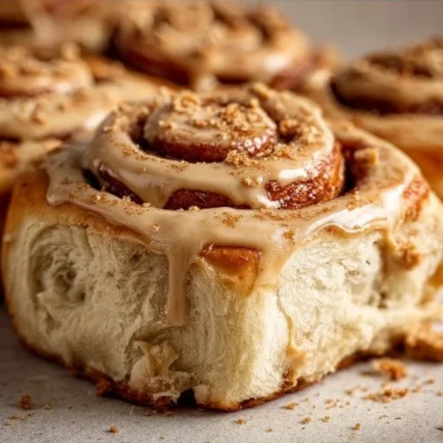 Biscoff cookie butter cinnamon rolls topped with icing on a white plate.