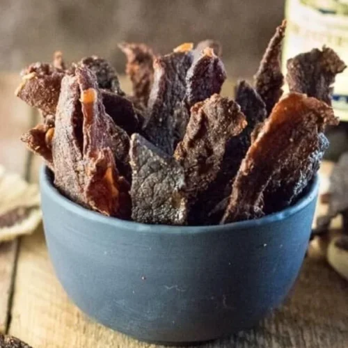 Homemade beef jerky drying on a tray with seasonings and spices